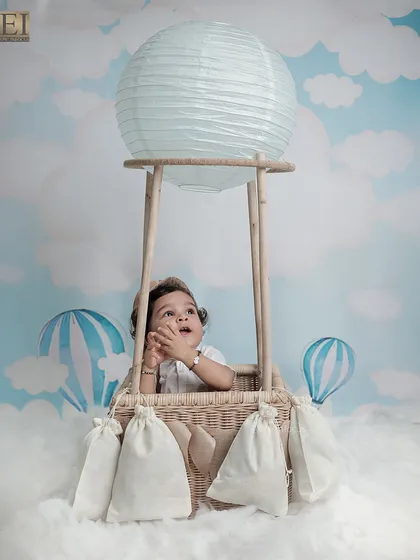 This little adventurer looks up in wonder from the basket of our hot air balloon prop, set against a dreamy sky backdrop.