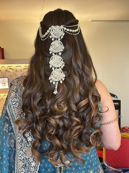A beautiful combination of open curls and a jeweled hairpiece. This half-up style keeps the hair away from the face while still showcasing its length and volume, perfect for an engagement or reception.