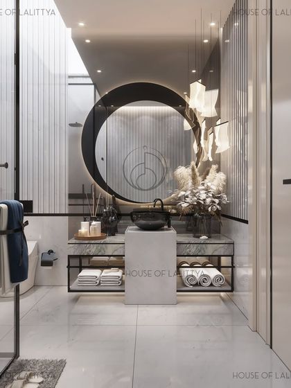 This bathroom design features a floating marble vanity with open shelving and a monolithic pedestal basin beneath a circular, illuminated mirror. Sculptural pendant lights cast a soft glow, complementing the fluted wall panels and creating a serene atmosphere.