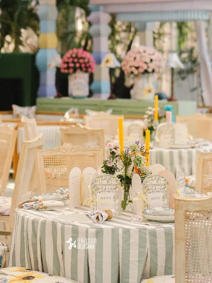 A dining table with a striped green and white tablecloth, topped with wildflowers and yellow candles.