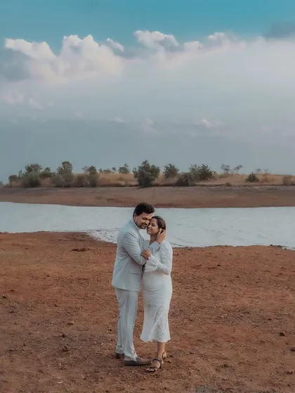A beautiful, wide shot of a couple embracing in an open landscape by the water, under a vast sky filled with clouds. This image captures a sense of peace and togetherness.