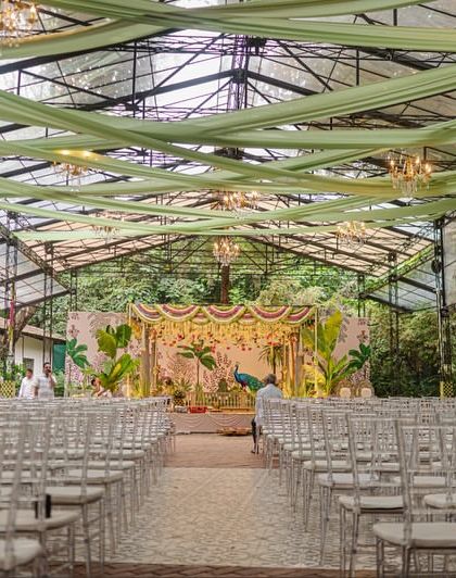 Another perspective of the glasshouse wedding venue, showing how the green ceiling drapes and chandeliers draw the eye towards the elaborate, traditional mandap. Every detail was planned to create a cohesive and immersive experience.