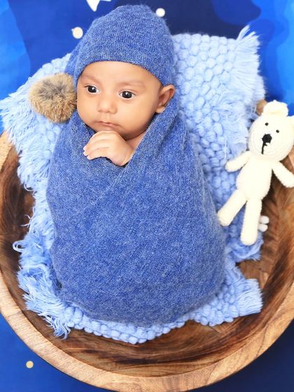 An awake moment during a "sweet dreams" session. The baby is swaddled in blue and looking thoughtfully from a wooden bowl, set against a dreamy, star-filled background.