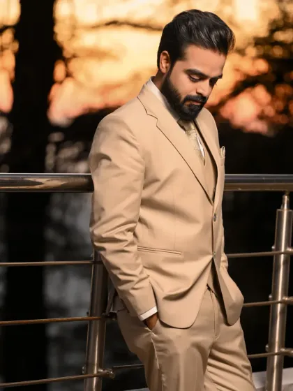 A classic, sophisticated portrait of the groom in a beige suit, looking down with a subtle smile. The warm sunset light adds a touch of elegance.