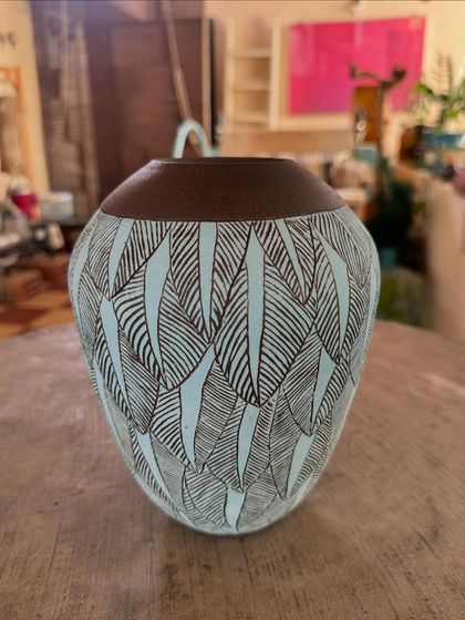 A closer look at a sgraffito vase with a leaf motif. The contrast between the dark clay body and the light-colored slip makes the hand-carved details pop.