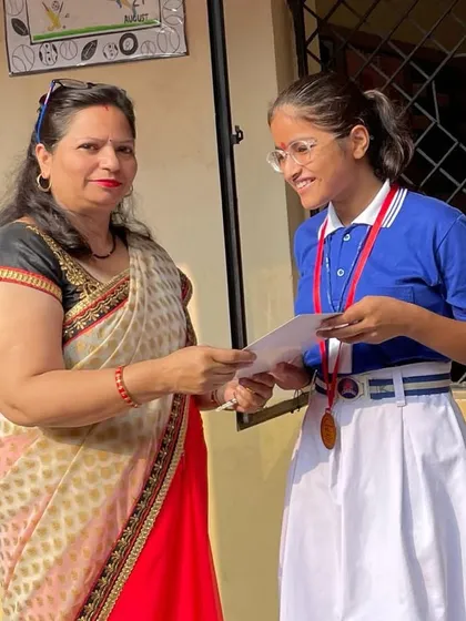 A student receiving her certificate and medal from her teacher. We work closely with schools to promote sports and recognize talent.