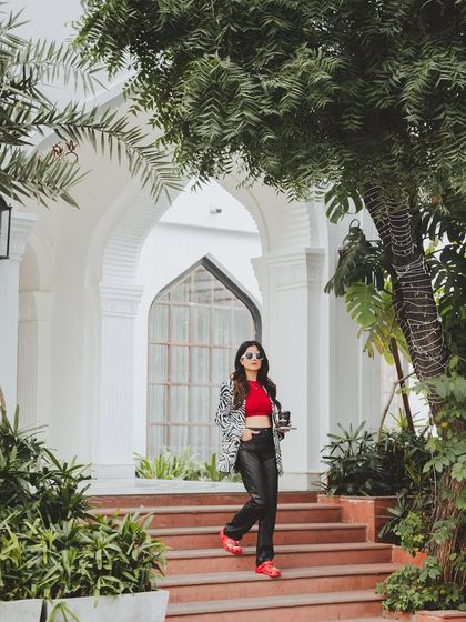A full-length shot in a beautiful, green outdoor setting. This image shows how the bold, red Crocs can be part of a stylish, everyday look, blending comfort with high fashion.