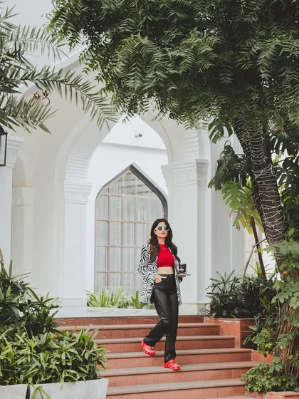 A full-length shot in a beautiful, green outdoor setting. This image shows how the bold, red Crocs can be part of a stylish, everyday look, blending comfort with high fashion.