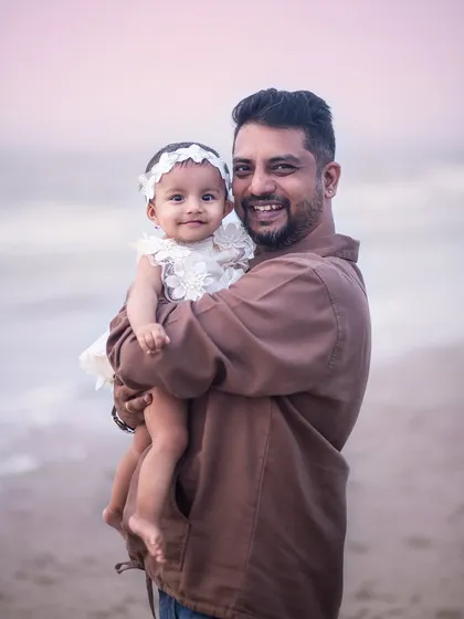 A proud father holds his adorable baby girl. This classic portrait at the beach is a beautiful keepsake of her early days.