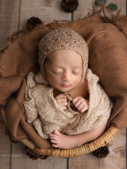 A two-week-old newborn wrapped in earthy brown tones, nestled in a basket. The textures of the knit bonnet and wrap add warmth and depth to the image.