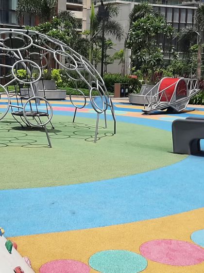 This playground at the Island City Center features a variety of modern play equipment on a colorful, soft-fall surface. The design includes a geodesic dome climber and a spinning rocker, providing diverse and engaging play opportunities for children.