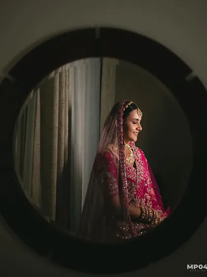 A creative shot of my bride Aayushii, captured through a mirror. The lighting is soft and highlights her serene expression and beautiful makeup.