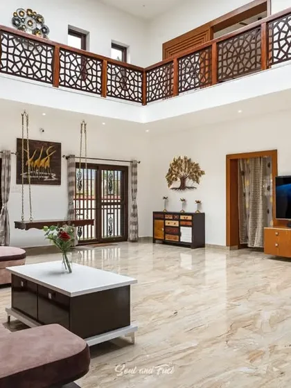 A grand, double-height living room with marble floors and a traditional wooden swing. The space feels expansive and luxurious, with a mezzanine level overlooking the main area.