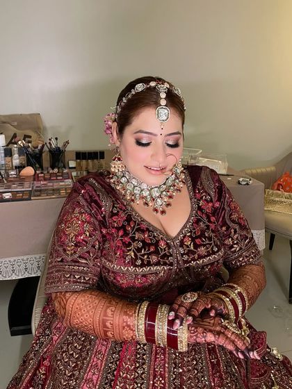 Juhi admiring her final look. The soft peachy tones on her eyes and cheeks create a warm, romantic glow that is perfect for a wedding day.
