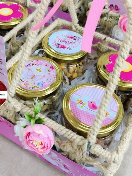 A top-down view of a jute announcement basket, showing the custom-designed lids on the treat jars, each with a unique pink floral or butterfly design.