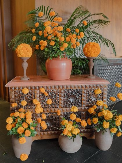 A decor detail featuring a carved wooden chest of drawers, beautifully styled with marigold arrangements.