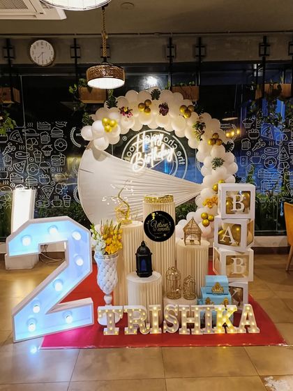 An elegant birthday setup in a restaurant, featuring a white balloon arch, marquee number '2', and 'BABY' blocks for a sophisticated toddler's party.