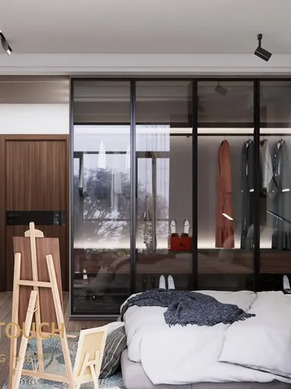 This modern bedroom features a striking marble accent wall behind the TV and a glass-paneled walk-in closet. The design mixes moody tones with reflective surfaces to create a sophisticated and spacious feel.