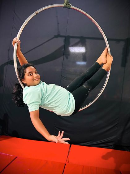 This young aerialist holds a seated pose in the hoop, demonstrating balance and building the foundational strength needed for more advanced moves.