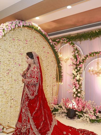 The bride posing in front of a beautiful floral backdrop. Her red lehenga and glamorous makeup stand out beautifully.