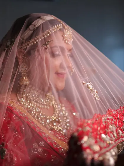 The classic bridal veil shot. The soft net veil adds a layer of mystique, while her glowing makeup and stunning jewelry peek through, creating a truly magical and timeless portrait.