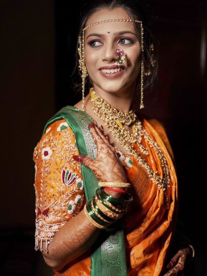 A beautiful bridal portrait, capturing her happy smile and the details of her orange and green saree.