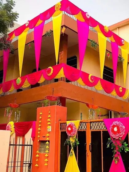 A vibrant and colorful house decoration using yellow and pink drapes with floral accents on the gate and balcony.