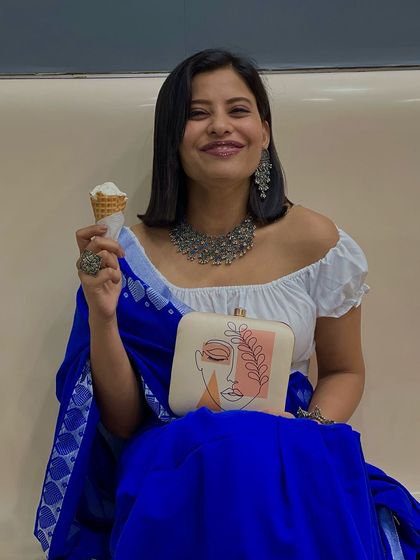 A full view of this chic and joyful ensemble. The clutch is held front and center, showing off its unique design while the customer enjoys a sweet treat. It's all about finding style in everyday moments.