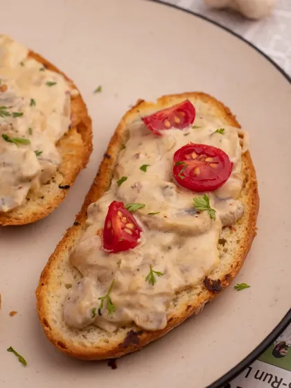 A close-up of creamy mushroom toast. This shot focuses on the texture of the creamy sauce and the freshness of the cherry tomato garnish.
