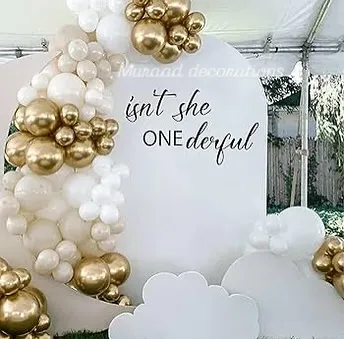 A sweet and simple setup for a first birthday. The backdrop reads 'Isn't she ONEderful' and is framed by a beautiful white and gold balloon garland, perfect for an elegant celebration.