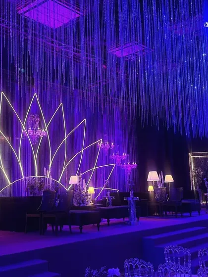 A view of the main stage and lounge area, showing the interplay of the neon lotus, crystal curtains, and sophisticated dark furniture. The design is a perfect example of modern luxury for a sangeet celebration.