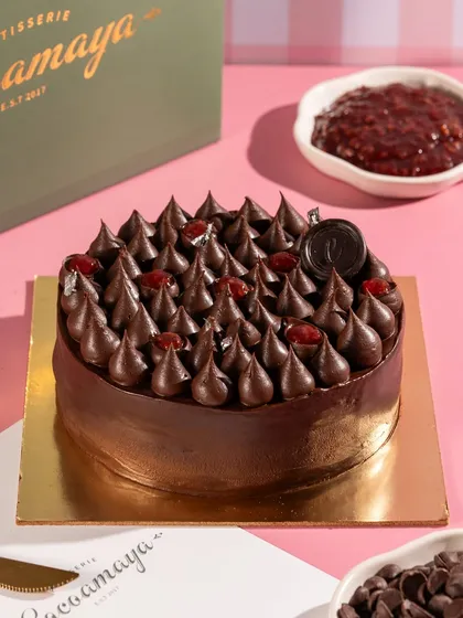 A full view of a chocolate drip cake, ready for a celebration. The styling with branded packaging makes it a great commercial shot.