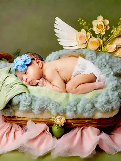 A one-month-old baby with angel wings sleeping in a teacup-shaped prop.