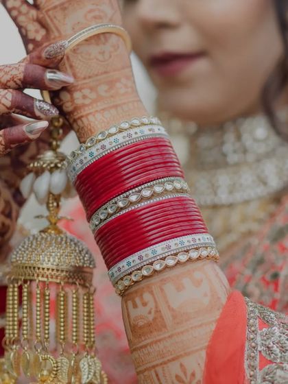 A detailed shot of the bride's hands, adorned with henna, red bangles (chooda), and traditional kalire.
