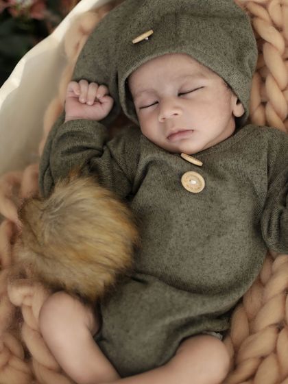 A detailed close-up of the baby's face and outfit from the 'hatching egg' photoshoot, showing the soft textures and cute button details.