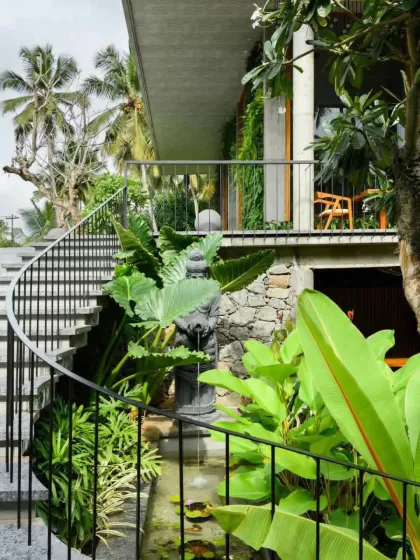 A spiral staircase is surrounded by a multi-level tropical garden featuring a small water feature. This design makes creative use of a tight space, turning a functional element into a beautiful garden moment.