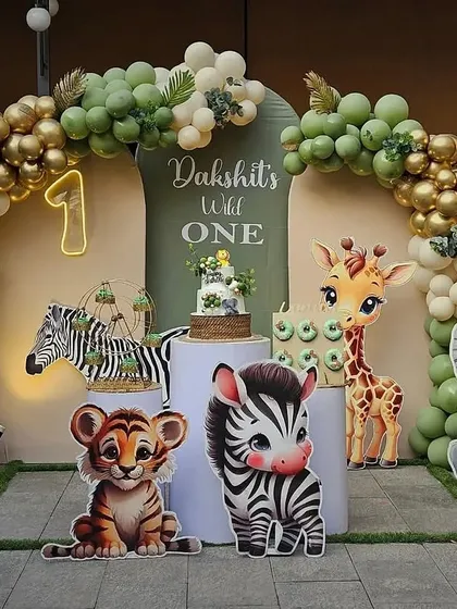 For little Dakshit's first birthday, we created a "Wild One" jungle safari theme. This adorable photo corner features cute animal cutouts, a lush balloon arch in sage green and gold, and a custom cake, setting the stage for a fun and memorable celebration.