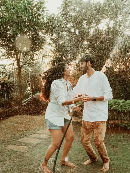 A candid shot of a couple laughing as they play with a water hose in a garden. This photo is filled with genuine joy and captures the fun, playful side of their relationship.