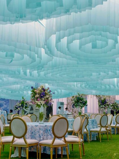 A wide view of the Dior-themed Mehendi setup, showing the cohesive design from the wavy fabric ceiling to the elegant guest seating and themed backdrops, all set on a lush green lawn.