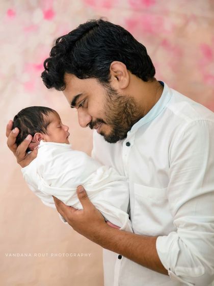 The bond between a father and his newborn is truly special. This tender moment, captured in a simple studio setting, shows a new dad gazing lovingly at his sleeping baby, a memory he will treasure forever.