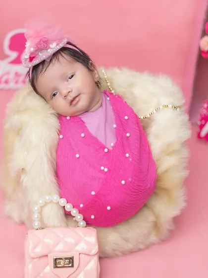 An awake newborn in a fun, pink Barbie-themed setup.