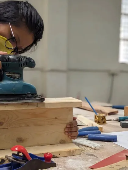 The final touches are just as important. Here, a participant uses a power sander to get a smooth, professional finish on her handmade pine wood box.