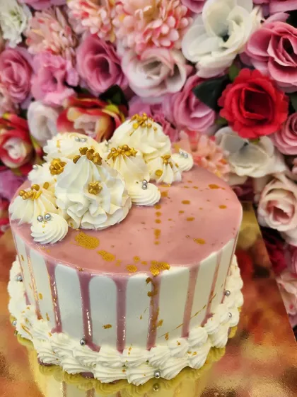 A beautiful White Truffle cake with a delicate pink drip. The top is adorned with swirls of cream and sprinkled with gold and silver pearls, giving it a touch of elegance and celebration.
