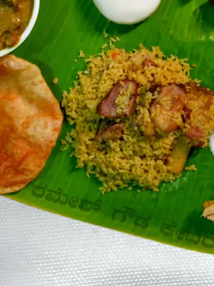A serving of our famous Mutton Biryani on a banana leaf, accompanied by a poori and raita. This is a classic combination loved by our clients.