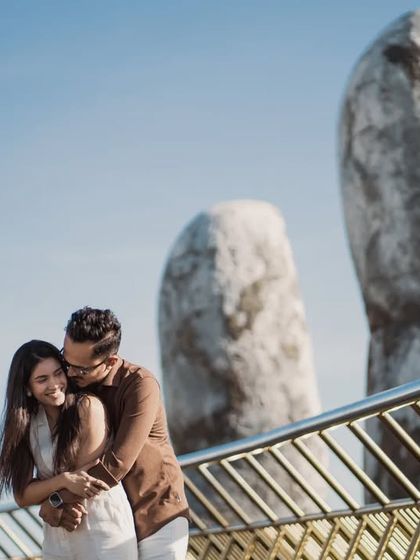 An intimate hug on Vietnam's Golden Bridge. The focus is on their happy expressions and the warmth of their embrace, with the iconic structure as a stunning backdrop.