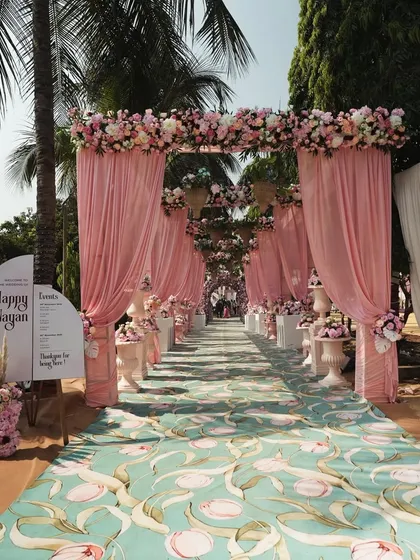 A wide view of the pastel pink themed wedding entrance. The draped fabric and floral arrangements guide guests down a beautifully printed aisle, setting a soft and romantic tone for the day.