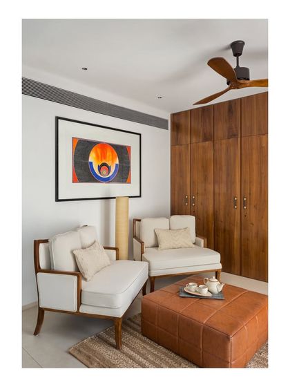 A seating area within the master bedroom of the House of Terraces. The combination of a leather ottoman, classic armchairs, and custom wooden wardrobes creates a space that is both functional and elegant.