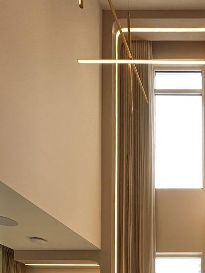 A detail shot of the custom lighting and architectural lines in the double-height living room. The linear chandelier and integrated cove lighting are designed to complement the verticality of the space.