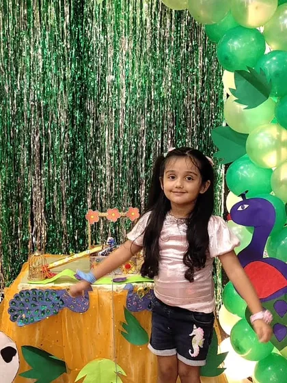 A young girl smiles brightly in front of our green and sparkly Janmashtami decor, ready to celebrate the festival of Krishna's birth.