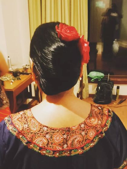 A sleek, low bun styled with a vibrant red flower. This is a simple yet striking look, ideal for a pre-wedding event or for a guest wanting a polished and elegant hairstyle.